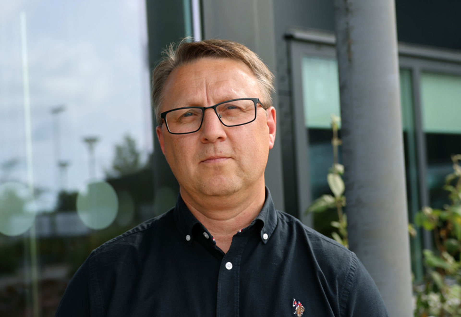 En man med glasögon som står framför en byggnad.